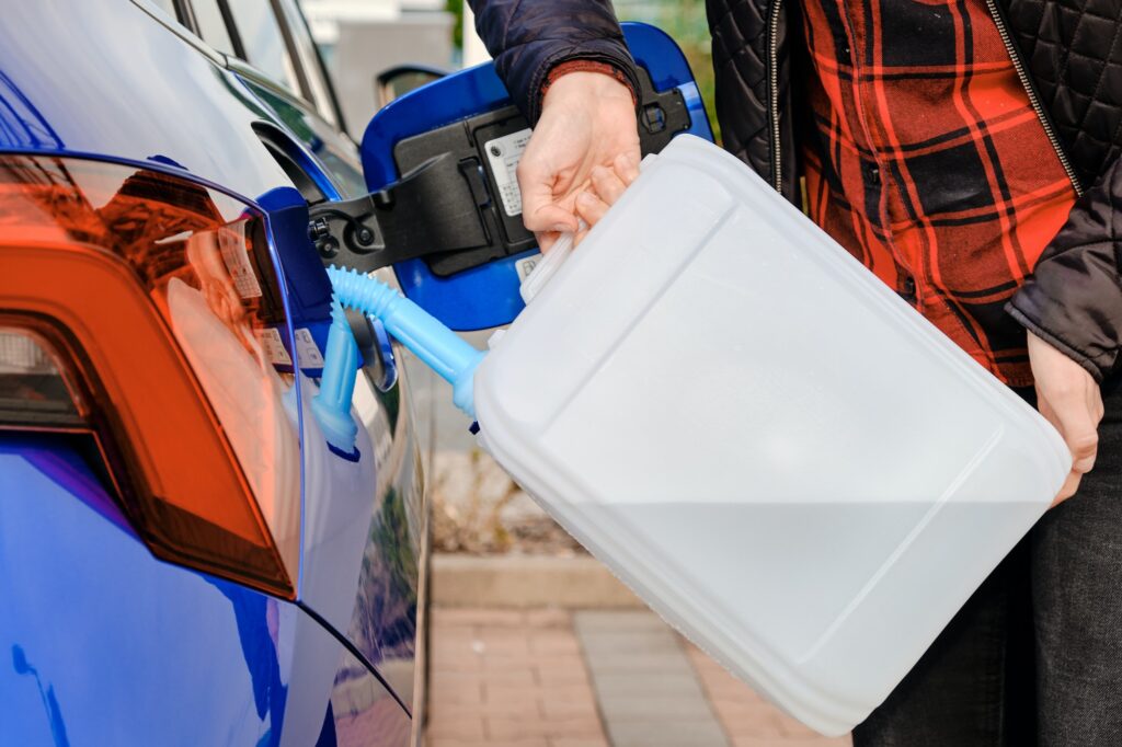Woman filling a diesel engine fluid from canister into the tank of blue car. Diesel exhaust fluid