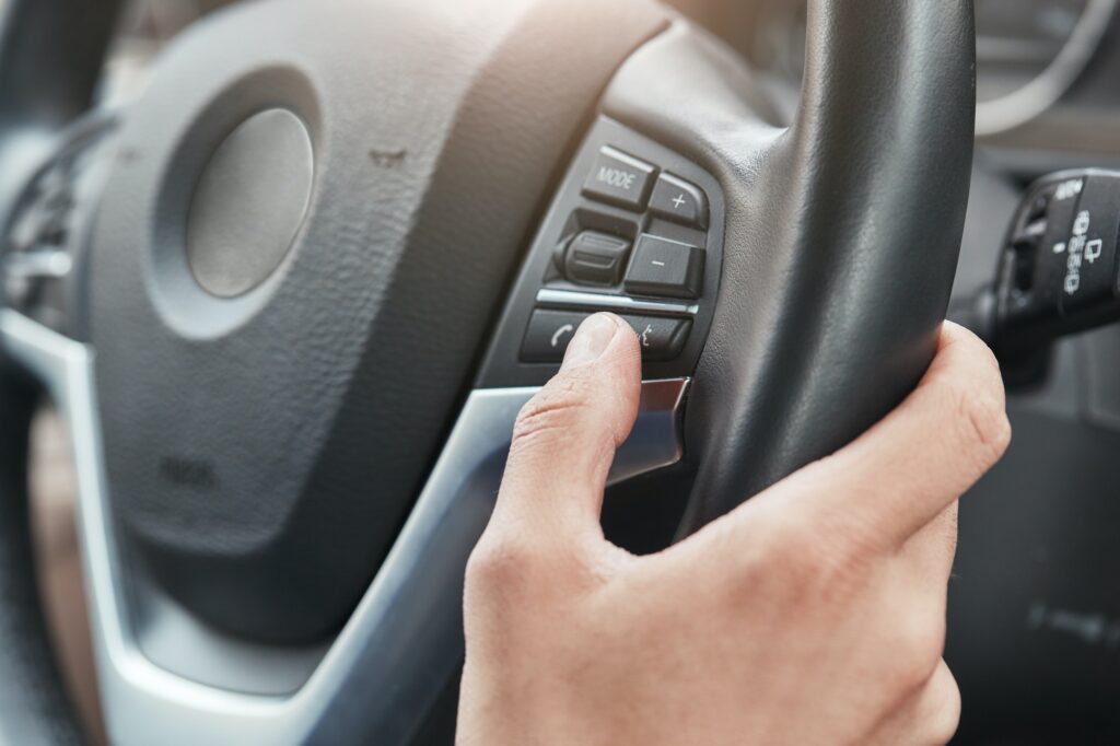 Cropped image of a hand pushing cruise control buttons on steering wheel in a modern car
