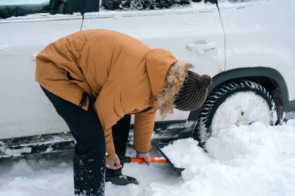 A man digs out a stalled car in the snow with a car shovel. Transport in winter got stuck