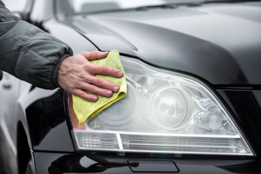 A man cleaning car's frontal headlights with microfiber cloth, car detailing concept.