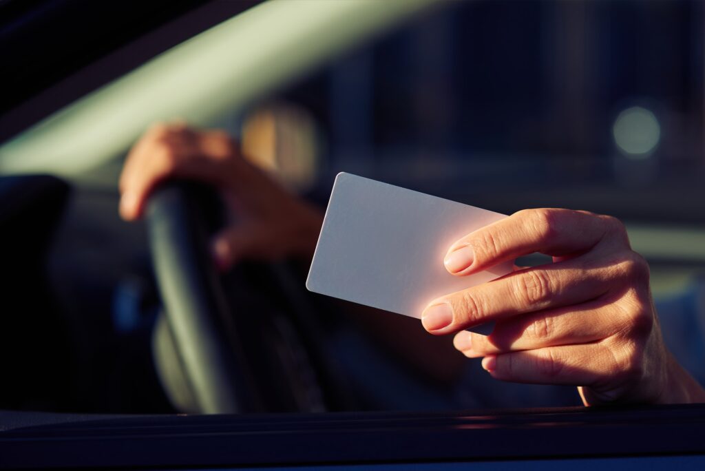 Close up shot of a female hand holding blank plastic card, woman sitting in car and showing license