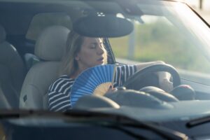Female driver with hand fan suffering from heat in car, has problem with non-working air conditioner