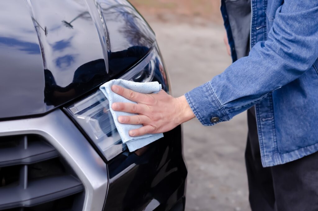 Male hand cleaning the headlights of a black car with a rag.