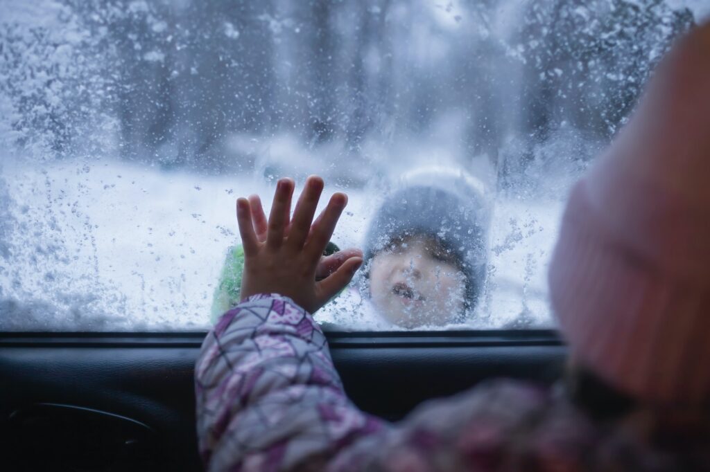 Boy and girl touch each other with palms through the frozen car window, winter family road trip