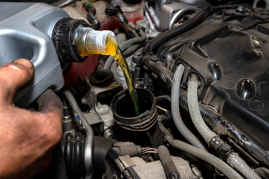 Car mechanic pours new car oil into the engine from a plastic tank in a car workshop.
